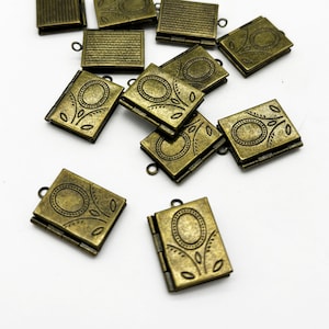 May include: A group of ten antique gold-toned metal locket charms in the shape of small books. Each locket has a hinged opening and a decorative design on the front.