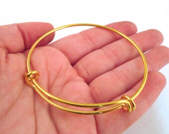 May include: A gold-toned bangle bracelet with a simple design. The bracelet is open and adjustable.