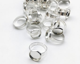 May include: A pile of silver-toned adjustable ring bases with round bezels. The bezels are empty and ready to be filled with resin, glass, or other materials.