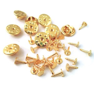 May include: A collection of gold-toned metal pin backs and safety pins. The pin backs are round with a textured surface and a small hole in the centre. The safety pins have a spring-loaded clasp and a pointed end.