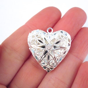 May include: A silver filigree heart-shaped locket pendant with a delicate floral design.