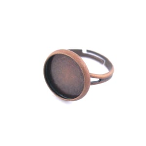 May include: A copper-toned ring with a round, empty bezel setting. The ring is adjustable and can be worn on any finger.