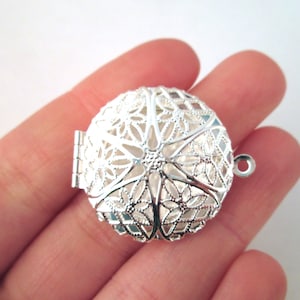 May include: Silver filigree locket with a hinged opening and a loop for attaching a chain. The locket is intricately designed with a floral pattern.
