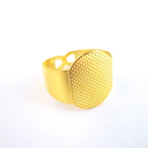 May include: A gold-colored thimble ring with a textured, dotted surface. The ring is designed to protect the finger while sewing. The ring is made of metal and has a simple, elegant design.