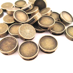 May include: A pile of round, antique gold-toned metal beads with a smooth, slightly textured surface. The beads have a hole in the center and are designed for jewelry making.