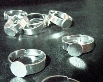 May include: A set of silver-toned adjustable ring blanks with round, flat, blank metal bases. The rings are made of metal and are designed to be used for crafting jewellery.