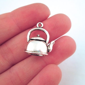 May include: Silver charm in the shape of a teapot. The teapot has a rounded body, a spout, and a handle. The charm is small enough to fit on a necklace or bracelet.