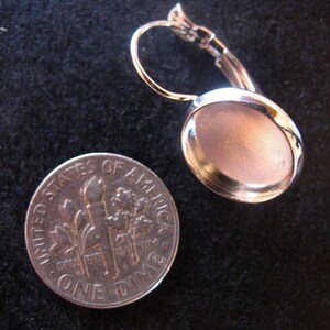 May include: Silver earring with a round, silver-toned bezel setting. The setting is approximately the size of a UK ten pence coin.