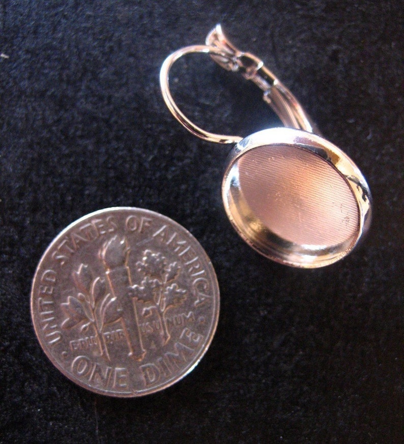 May include: Silver earring with a round, silver-toned bezel setting. The setting is approximately the size of a UK ten pence coin.