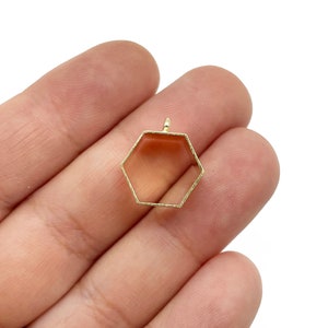 Op de afbeelding: Gouden metalen hexagonale hanger met een gladde, gepolijste afwerking. De hanger heeft een lus aan de bovenkant om aan een ketting of koord te bevestigen.
