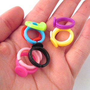 May include: A collection of colorful plastic rings, some with a flat base, in various colors including pink, yellow, black, green, blue, and purple.