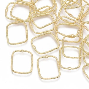 May include: A pile of gold-colored metal square jump rings with a textured finish. The jump rings have a small loop at the top for attaching to other jewelry pieces.