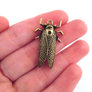 May include: A gold-toned metal charm in the shape of a cicada insect. The charm has detailed wings and a textured body.
