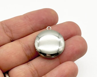 May include: A small, round, silver-colored locket with a smooth, reflective surface. The locket has a small loop at the top for attaching to a chain or necklace. The locket is shown against a white background.