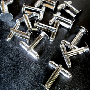 May include: A group of silver cufflinks with a round, flat back. The cufflinks are arranged in a random pattern on a black surface.