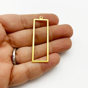Pode incluir: Um pingente de metal dourado em forma de retângulo com um pequeno laço no topo.