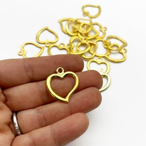 May include: A pile of gold-colored metal heart-shaped charms with a loop at the top. The charms are about 1 inch in size.