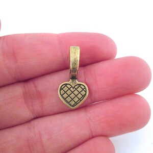 May include: A gold-toned heart-shaped metal pendant with a textured design. The pendant has a loop at the top for attaching to a chain or cord.