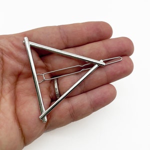 May include: Silver triangle hair clip with a simple design. The clip is made of metal and has a smooth finish.