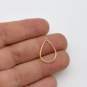 May include: A gold-colored teardrop-shaped pendant with a small loop at the top for attaching to a chain or earring hook. The pendant is made of a thin, smooth metal and is displayed against a white background.