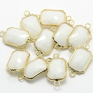May include: Ten white rectangular glass charms with gold-toned metal frames and double jump rings. The charms have a faceted design.