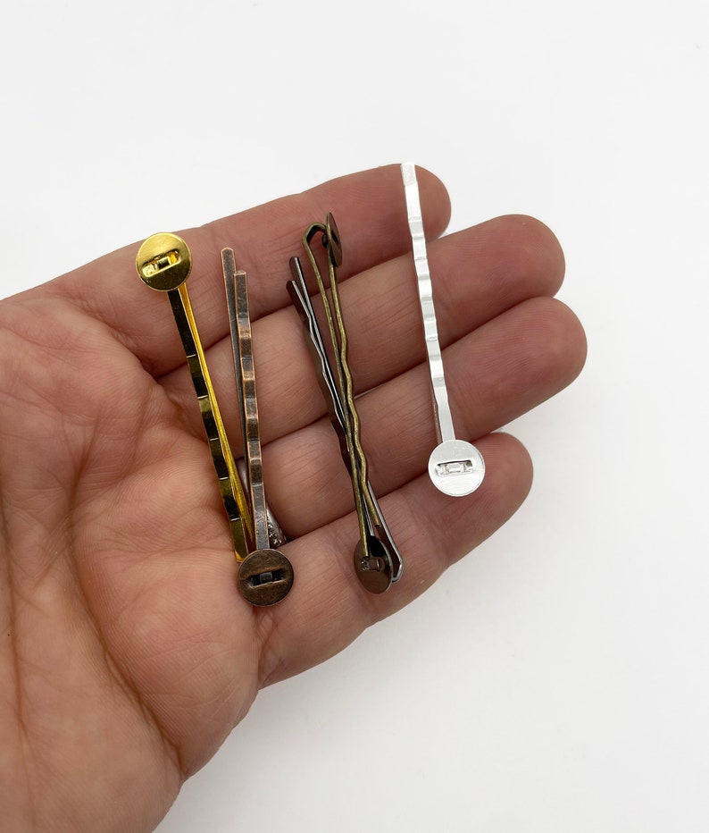 May include: Four hair clips with different finishes: gold, bronze, silver, and a wavy bronze clip. Each clip has a round button on the end.