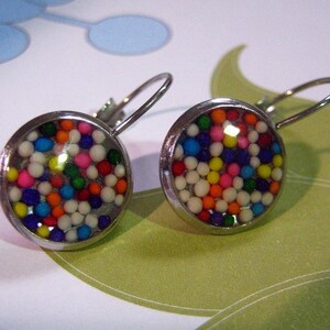 May include: A pair of silver earrings with round, clear glass fronts filled with colourful sprinkles. The sprinkles are a mix of white, red, orange, yellow, green, blue, and purple.
