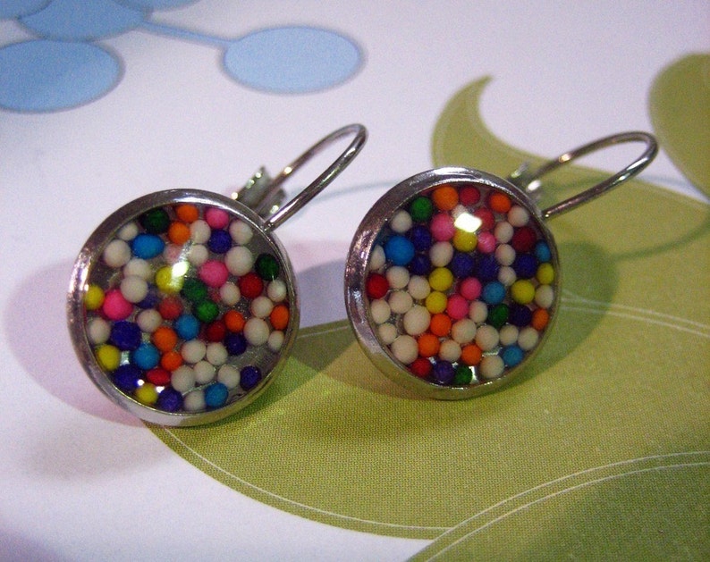 May include: A pair of silver earrings with round, clear glass fronts filled with colourful sprinkles. The sprinkles are a mix of white, red, orange, yellow, green, blue, and purple.