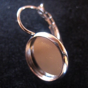 May include: Silver earring with a round, flat, silver bezel for a cameo or other embellishment.