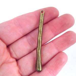 May include: A long, thin, gold-colored metal pendant with a rounded end and a small hole at the top.