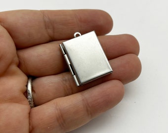 May include: A silver-toned locket pendant with a hinged opening. The locket is rectangular in shape and has a smooth, polished finish.