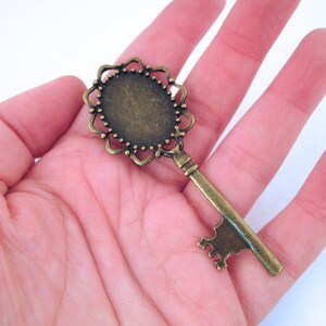 May include: A bronze-colored key with a decorative, ornate head. The head is oval-shaped and has a raised, scalloped edge. The key is about 3 inches long.