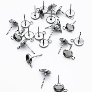 May include: A group of silver-toned earring settings with round bezels and a loop on the side. The settings are designed to hold a cabochon or other decorative element.