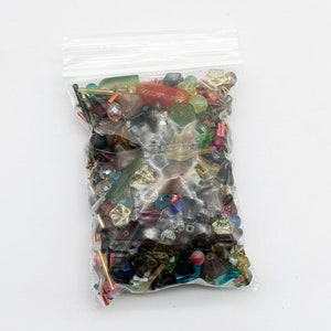May include: A clear plastic bag filled with a variety of colorful beads. The beads are made of glass and plastic and come in a variety of shapes and sizes. The beads are a mix of red, green, blue, yellow, and clear.