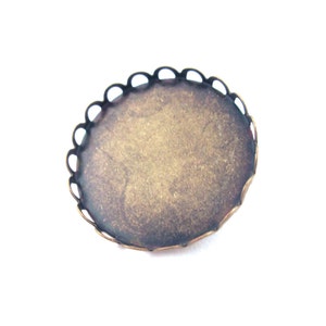 May include: A round, gold-toned metal tray with a scalloped edge. The tray is designed to hold a small round object, such as a cameo or a coin.