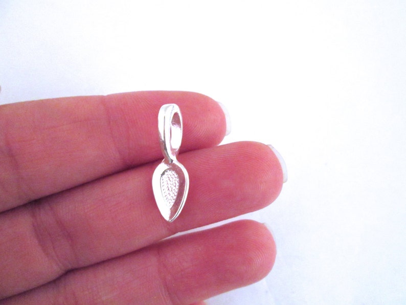 May include: Silver pendant bail with a teardrop shape and a loop at the top.