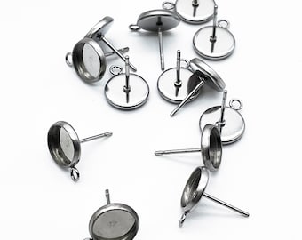 May include: A group of silver-toned earring settings with round bezels and posts. The settings are scattered on a white surface.