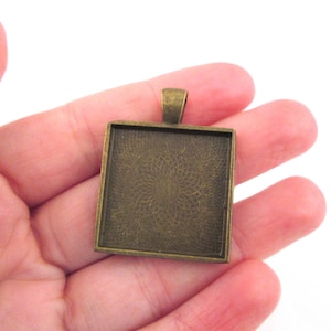 May include: A square-shaped pendant tray made of bronze metal with a textured surface. The tray has a loop at the top for attaching a chain.