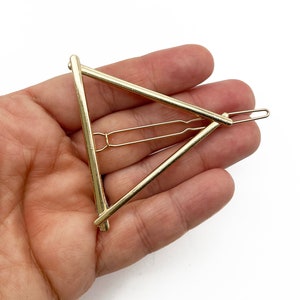 May include: Gold triangle hair clip with a simple design. The clip is made of metal and has a smooth finish.