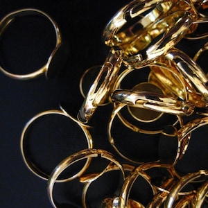 May include: A close-up of a pile of gold-colored metal rings. The rings are all different sizes and shapes, and they are arranged in a random pattern. The rings are shiny and reflect the light.