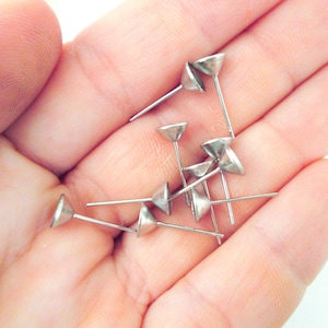 May include: A close-up of a hand holding a pile of silver-toned, cone-shaped, metal tacks with sharp points.