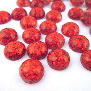 May include: A group of red glitter cabochons, round and flat, with a shiny, sparkly finish.