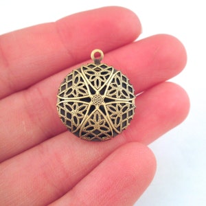 May include: A gold-toned metal pendant with a circular, intricate, filigree design. The pendant has a loop at the top for attaching to a chain or cord.
