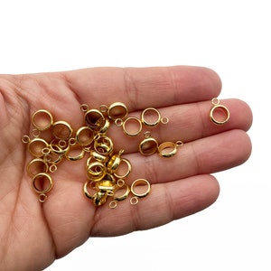 Puede incluir: Un montón de anillos de salto de metal dorado con un pequeño bucle en cada anillo. Los anillos están esparcidos en una mano.