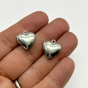May include: Two silver heart-shaped locket charms with a hinged opening. The charms are shown in a hand.