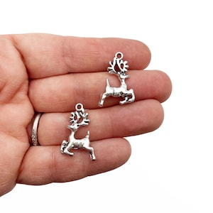 Op de afbeelding: Twee zilveren rendierbedels in een springende pose met gewei. De bedels hebben een glanzende afwerking en zijn perfect om sieraden of knutselwerk een feestelijke touch te geven.