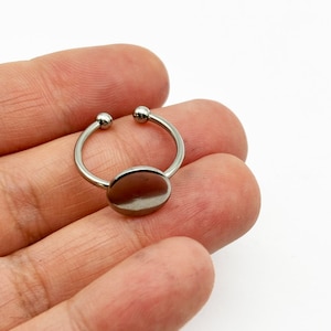 May include: A silver ring with a round, flat, silver disc in the center. The ring is open on one side and has two small silver balls on the ends.