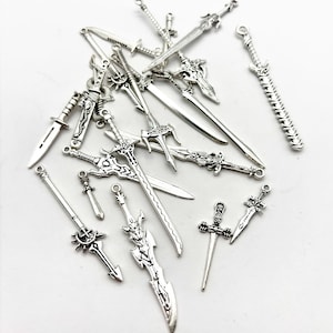 May include: A collection of small, silver-colored sword charms in various designs. The charms include detailed miniature swords, daggers, and decorative blades, perfect for jewelry making or crafting projects. The charms are scattered on a white surface.