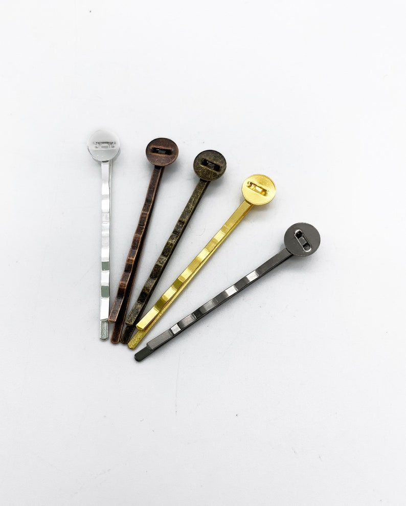 May include: Five hair clips with different colored metal tops. The clips are silver, bronze, gold, and two shades of gray.