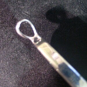 May include: Close-up of a silver metal loop with a smooth, rounded surface. The loop is part of a larger object, possibly a piece of jewelry or a decorative element.